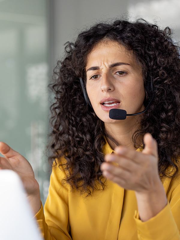Serious and focused woman with headset talking remotely, close-up of helpline worker working remotely, using laptop for video call, at workplace inside office