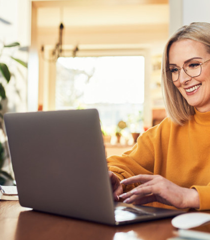 Mujer sonriendo mientras usa un portátil en interior.