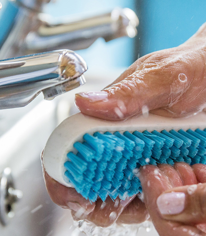 Cepillo azul limpiando dedos junto a un grifo.