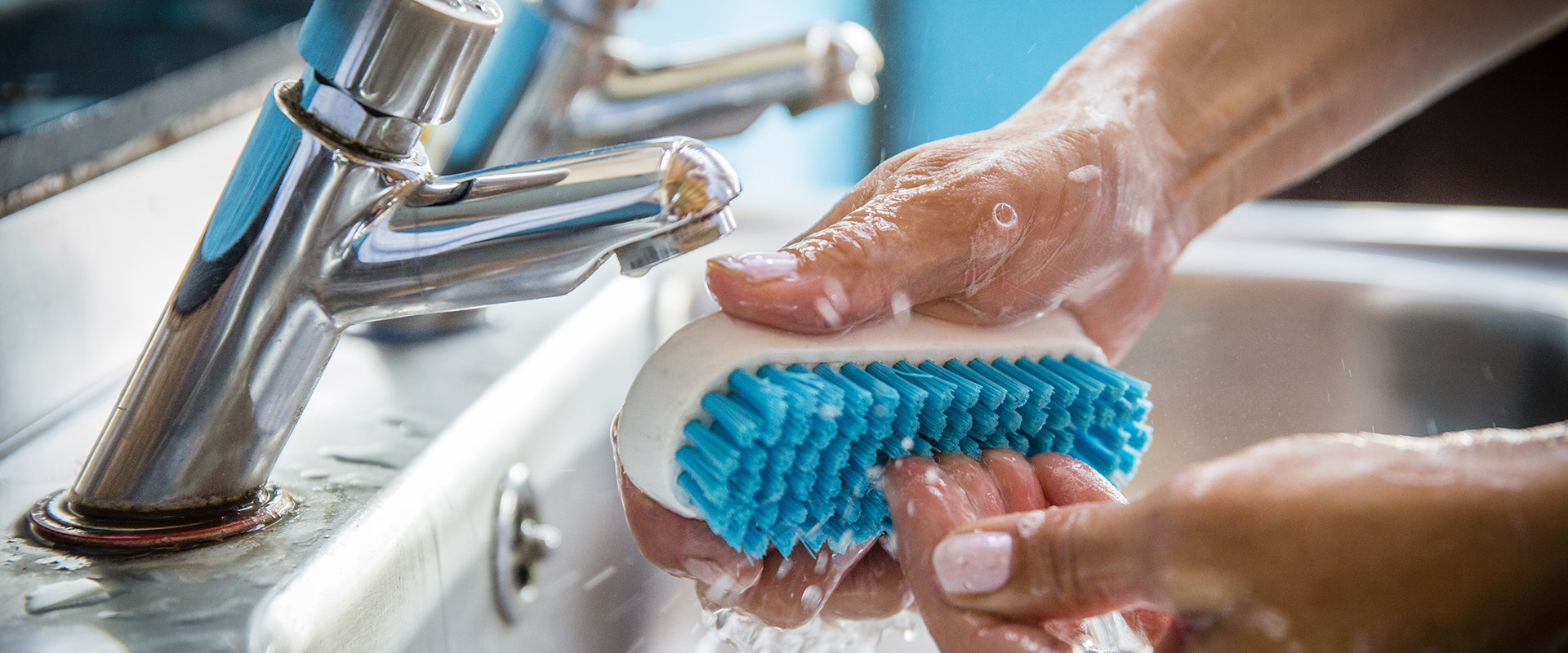 Cepillo azul limpiando dedos junto a un grifo.